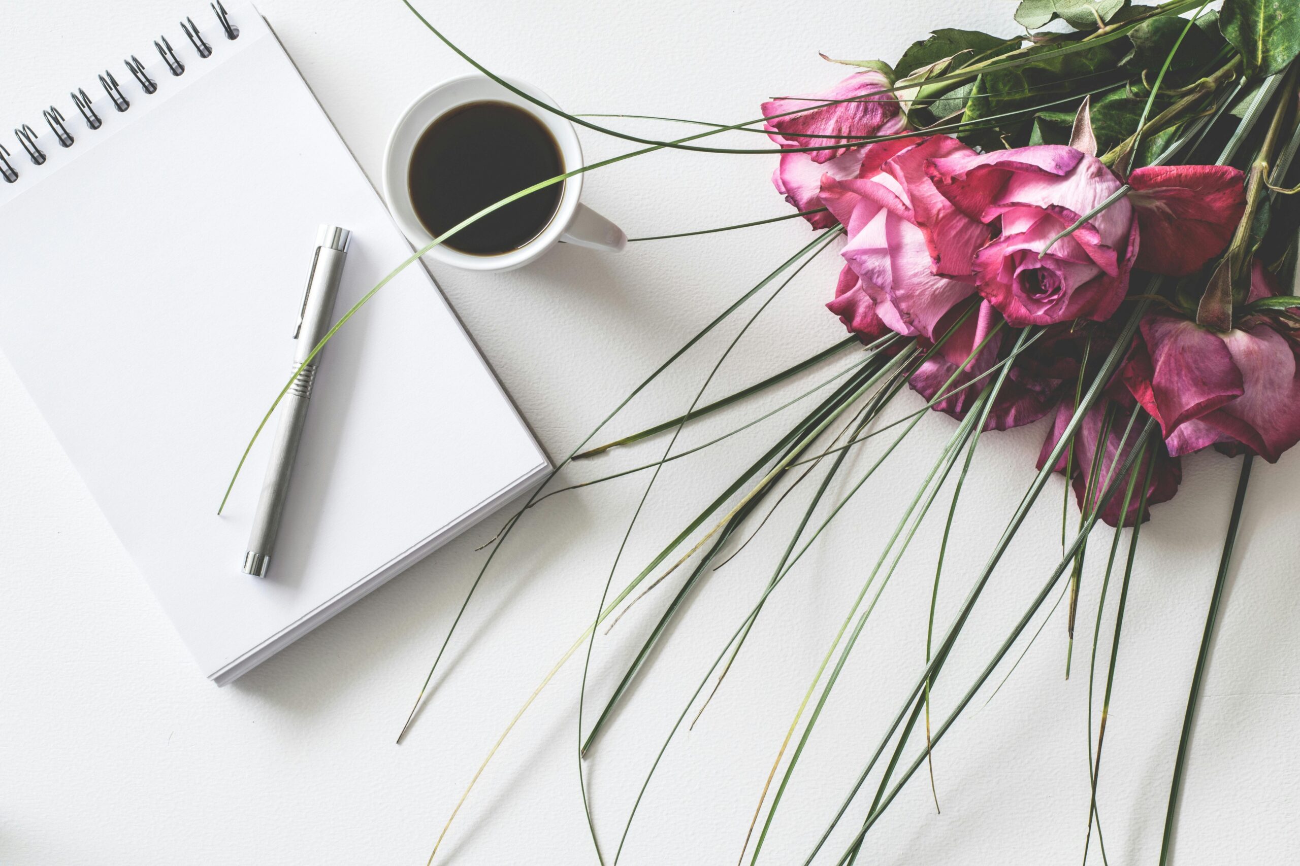 open notepad planner with a pen and coffee next to pink roses